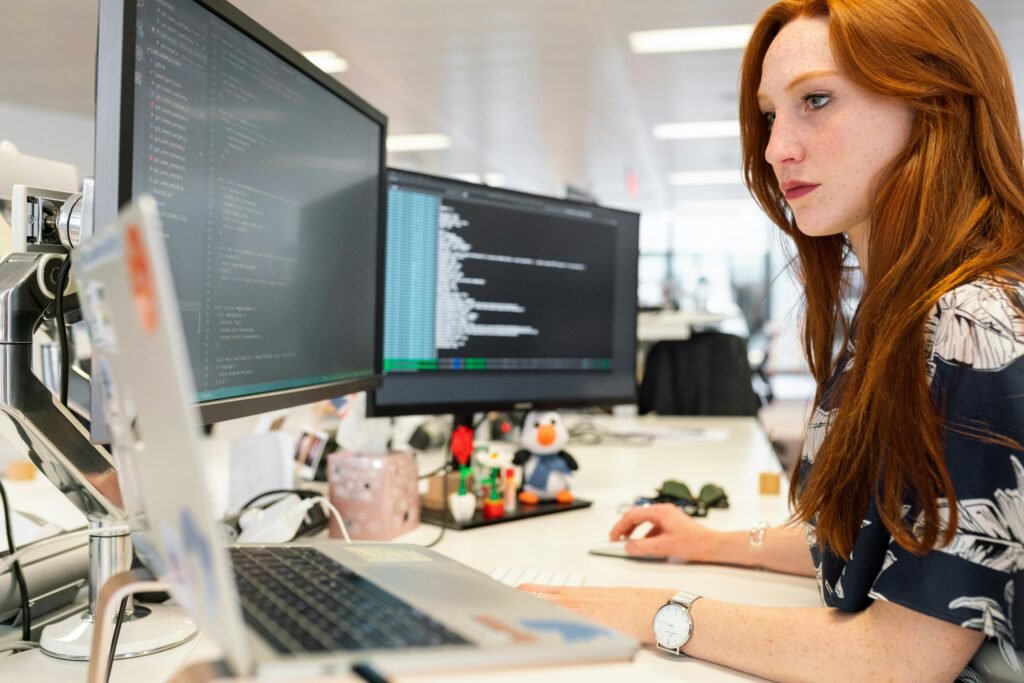 A focused female software engineer coding on dual monitors in a modern office -